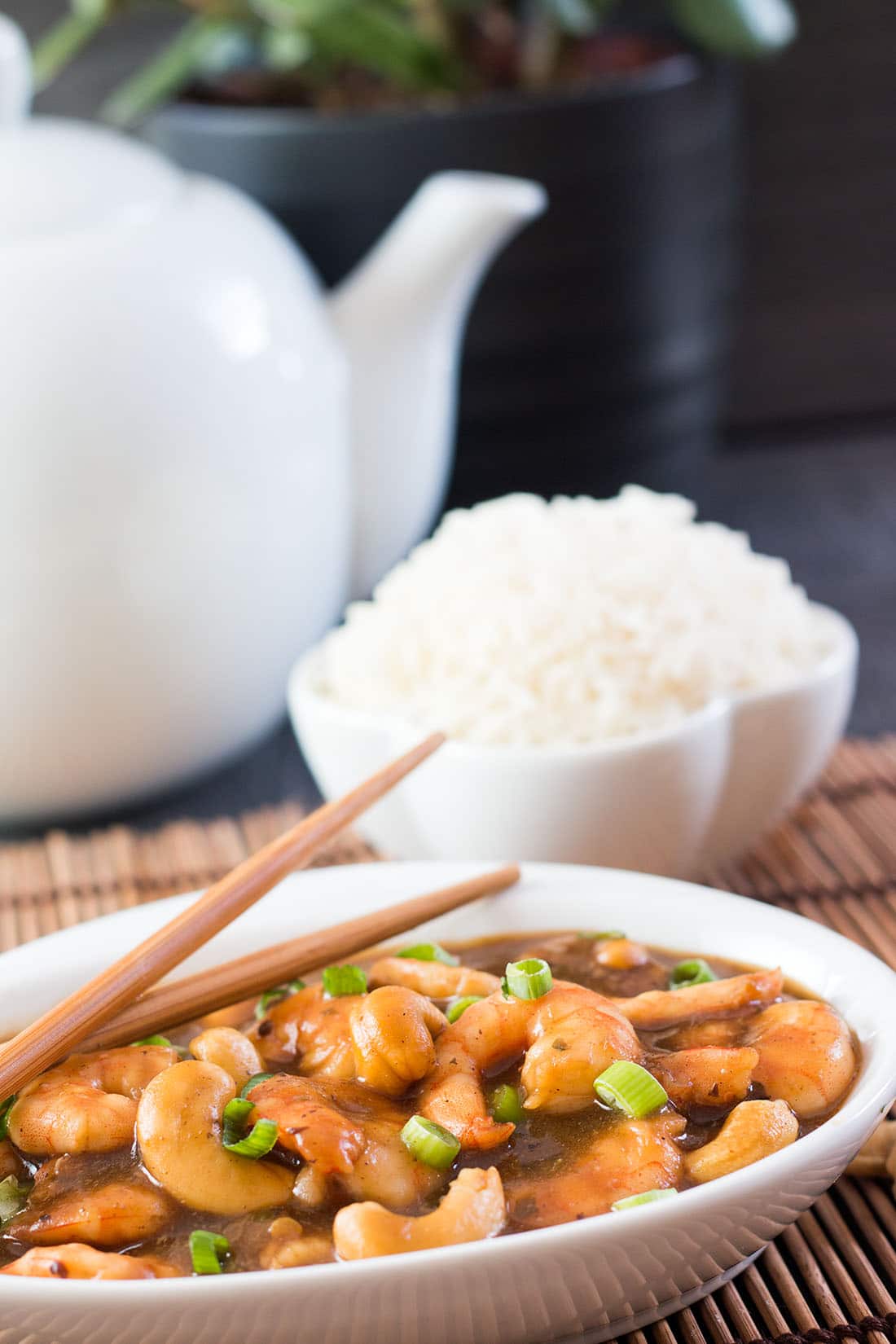 Cashew shrimp, rice in a bowl with a white teapot in the background.