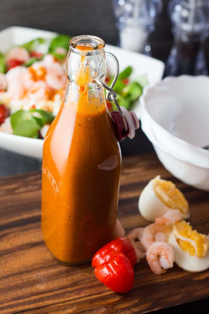 Catalina Style Peppadew Salad Dressing in a bottle with garlic, shrimps and peppers next to it