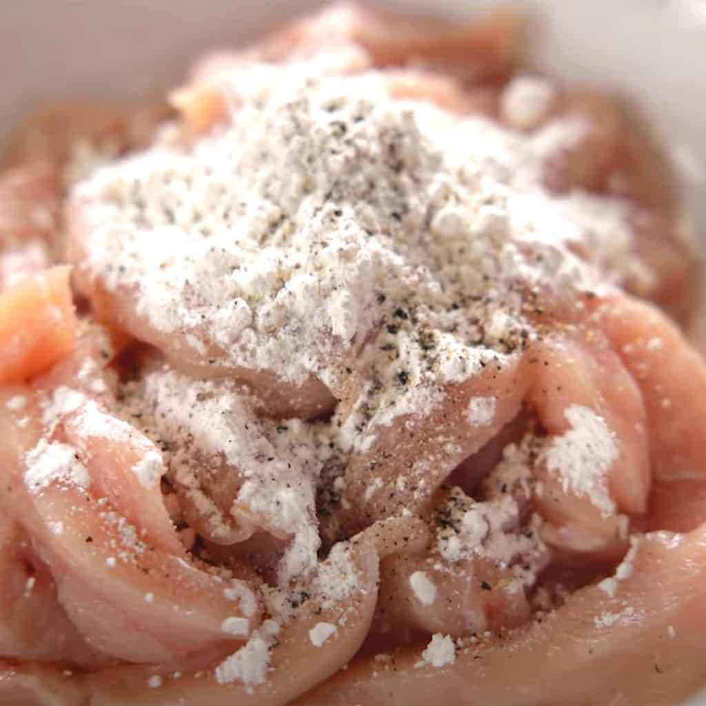 chicken with salt, pepper, and cornflour in a bowl