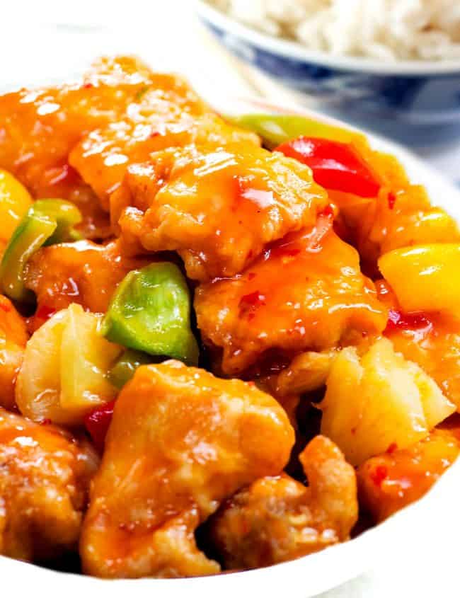 a bowl full of Sweet and sour chicken with white rice in the background