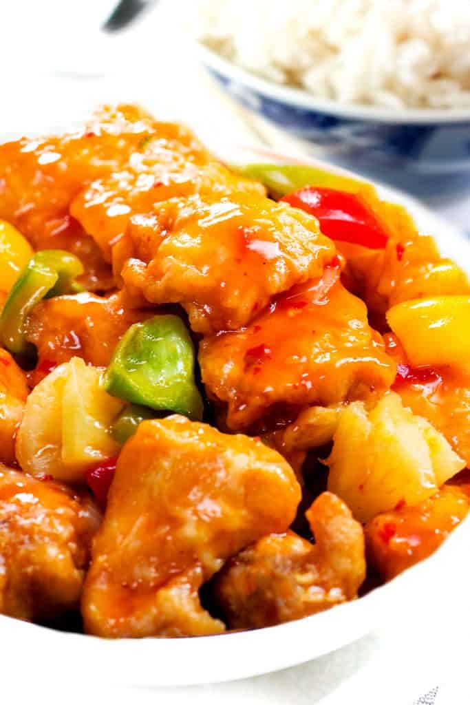 a bowl full of Sweet and sour chicken with white rice in the background