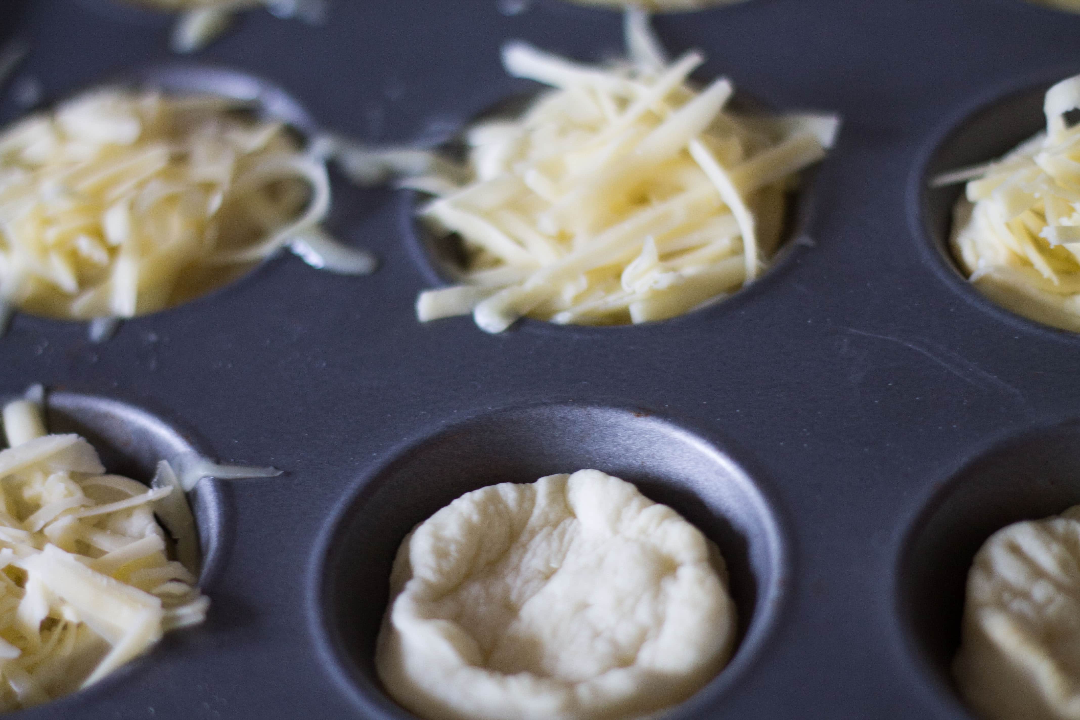 raw pie crust teopped with cheese in a tartlet pan