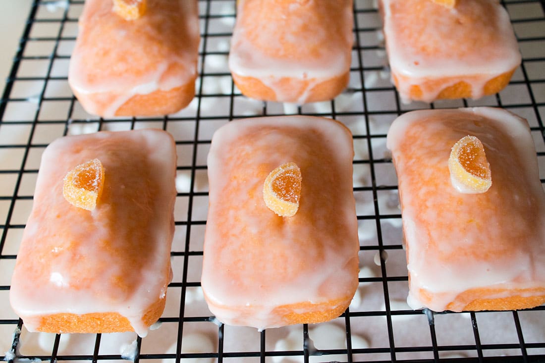 Mini Glazed Orange Cakes lined up on a cooling rack with candied orange slices on to of each one as decoration