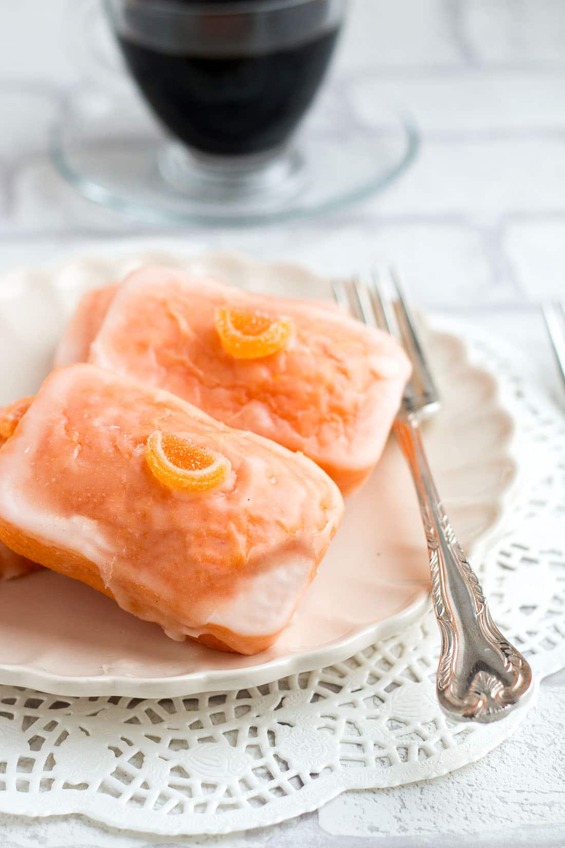 Orange Glazed Cakes on a plate with a fork and a cup of coffee in the background