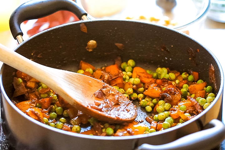 The peas added to the vegetables and spices in the pan