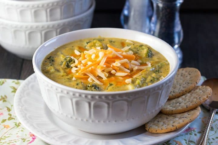 A bowl of thick, vibrant soup with chucks of broccoli and shredded white and orange cheddar cheese on top