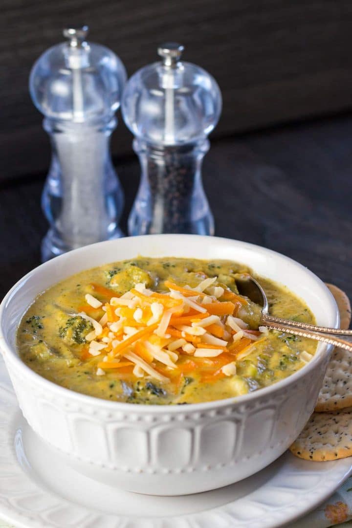 A bowl of thick, vibrant soup with chucks of broccoli and shredded white and orange cheddar cheese on top.