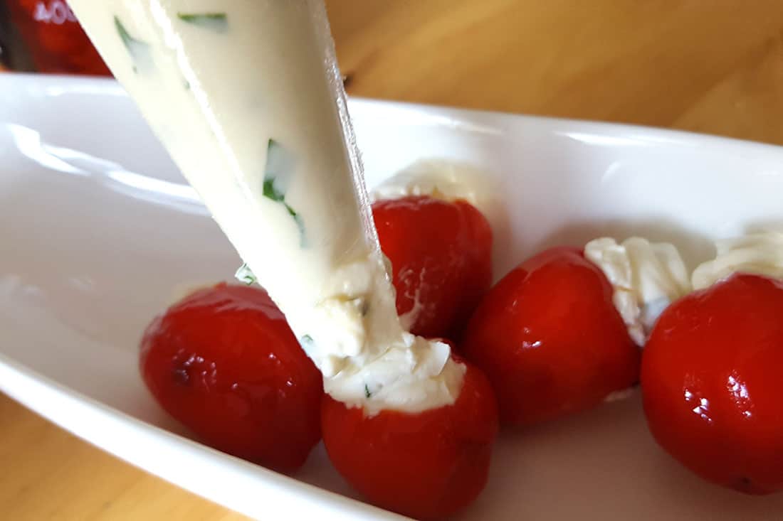 A bowl of peppadews being piped with cream cheese filling