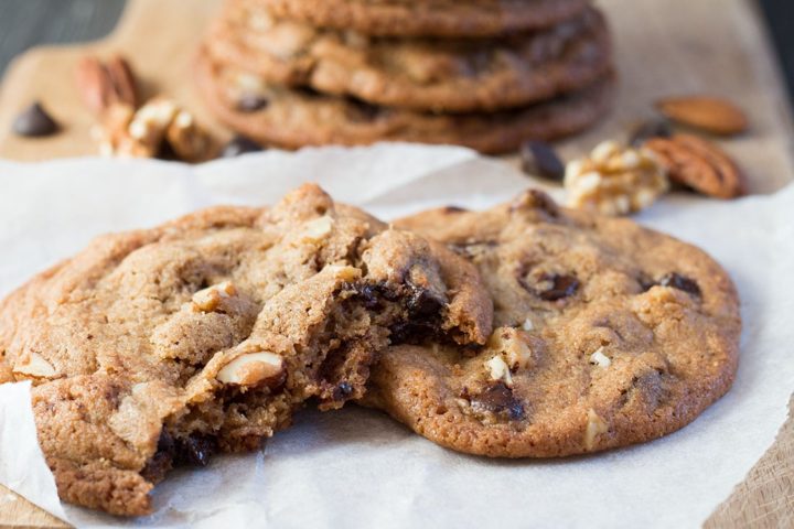 Nutty Chocolate Chip Cookies on a napkin with one broken in half showing nuts and chocolate