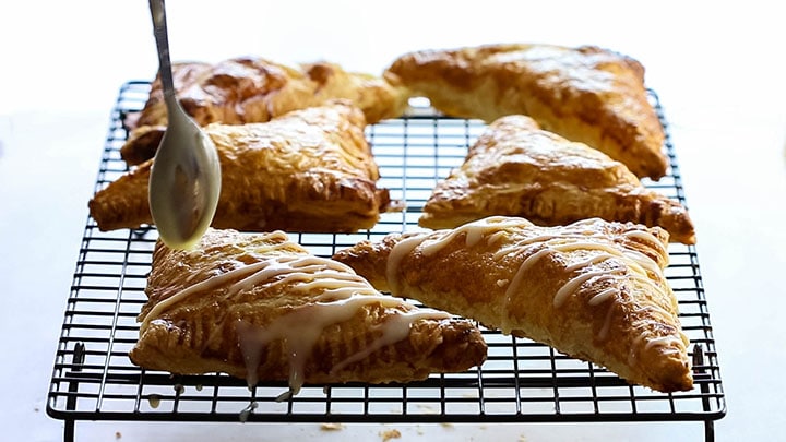 Apple turnovers on a cooling rack drizzled with icing.