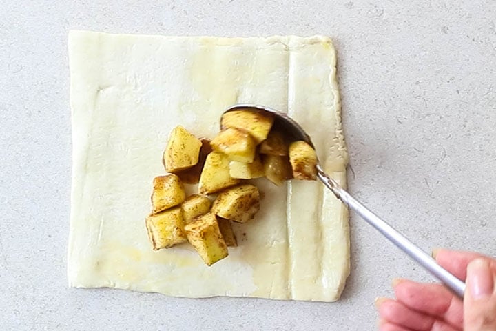 Apple mixture being spooned onto puff pastry dough