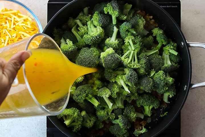 The stock being poured over the broccoli in the pan