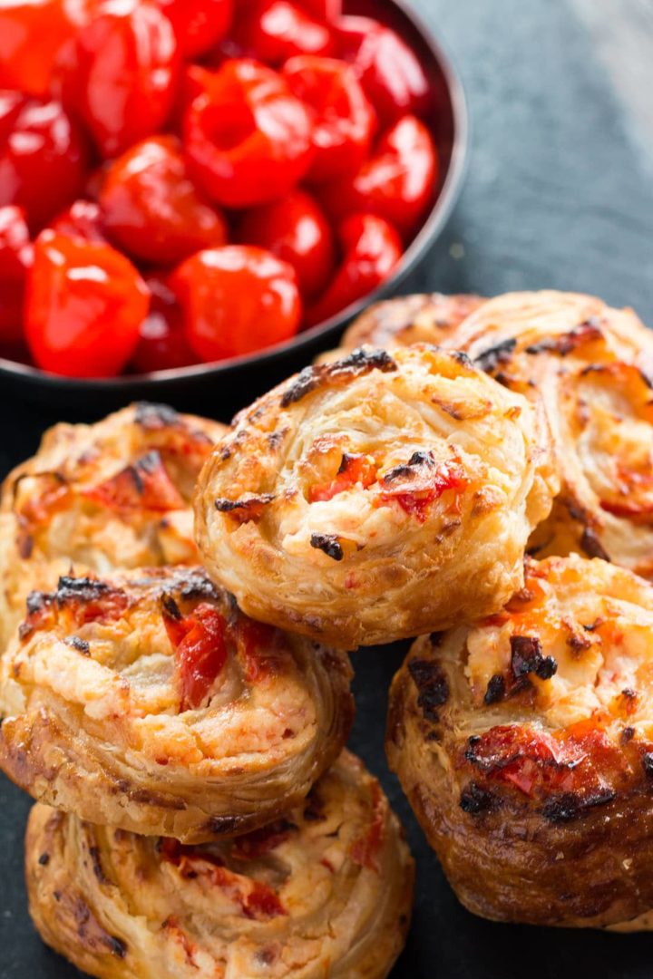 Feta & Sweet Pepper Pastry Swirls in a pile with a bowl of peppers in the background