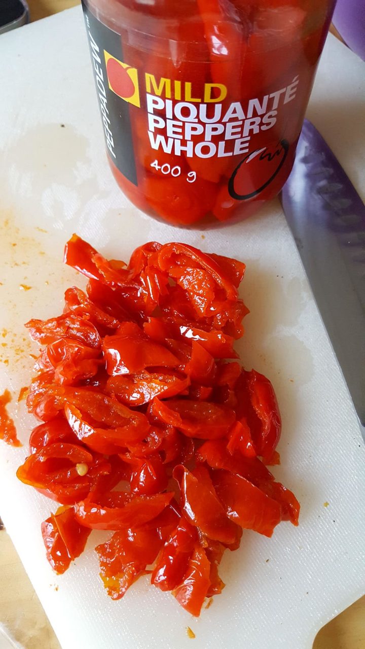 chopped mild piquante peppers on a white chopping board with a jar of peppers in the background