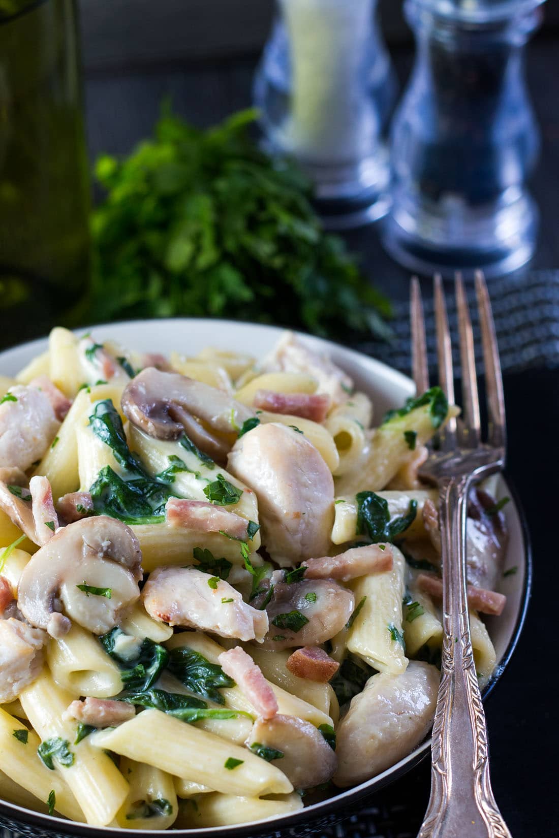 The Creamy Chicken and Bacon Pasta close up with a fork in the bowl and salt and pepper in the background.