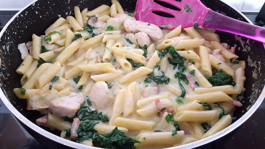 A pan with Creamy Chicken and Bacon Pasta cooking with a spatula mixing.