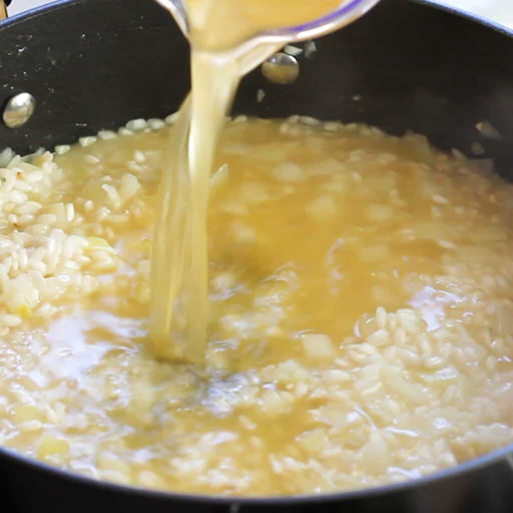 stock being poured into the pan with the rice mixture