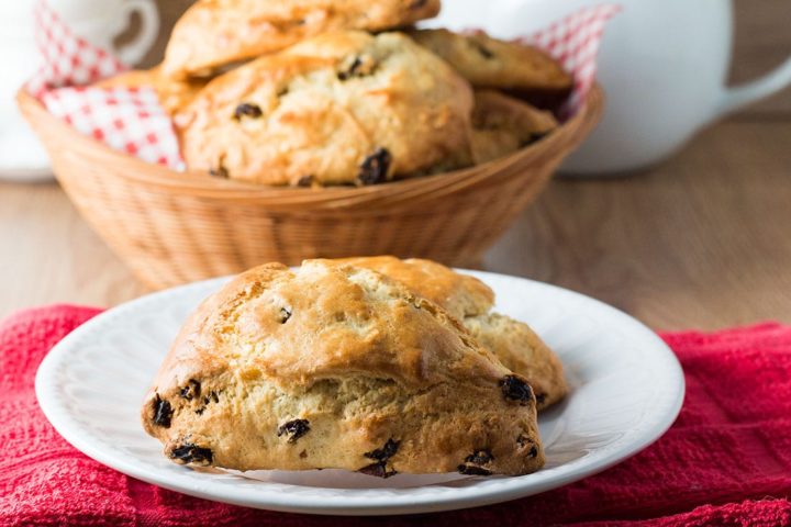 Raisin Scones on a white plate with a basket of scones in the background