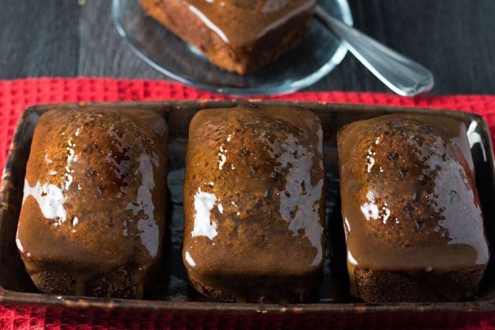 Three Sticky Toffee Ginger Cakes on a serving plate side by side covered in the shiny glaze