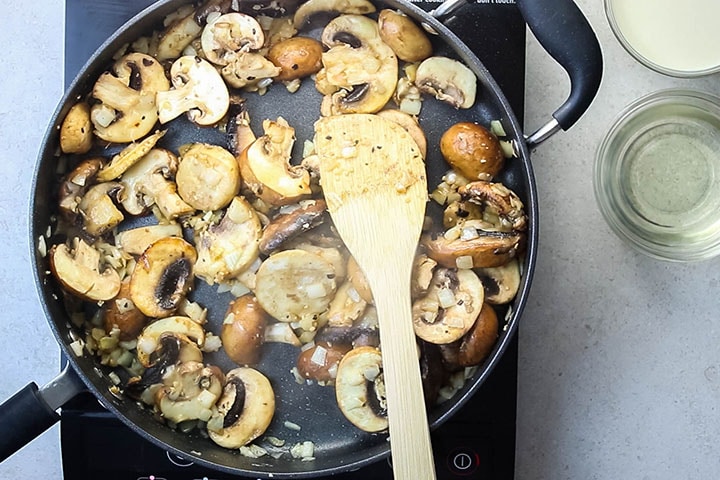 A pan with mushrooms sauteing with onions and garlic.