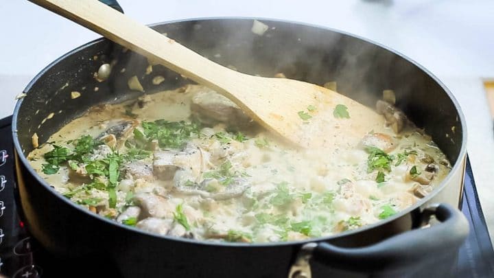 A pan with mushrooms in a bubbling cream sauce with parsley