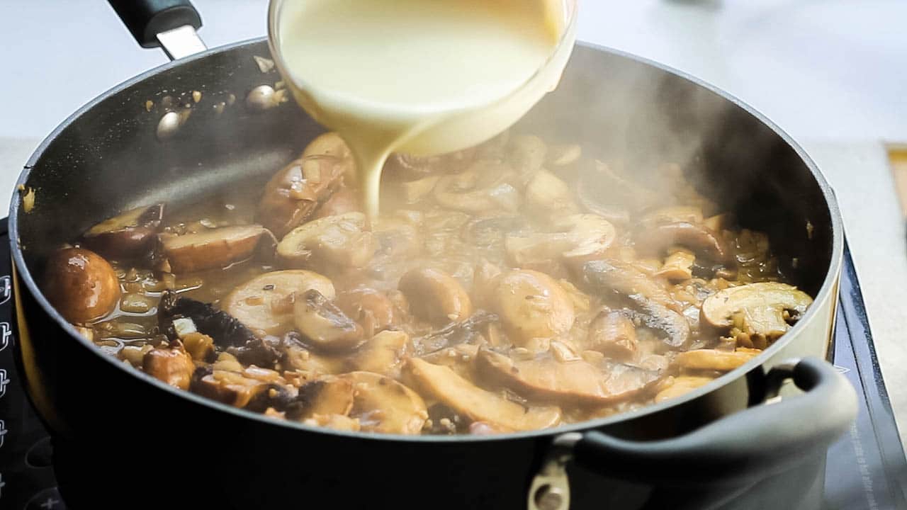 A pan with mushrooms and cream being added