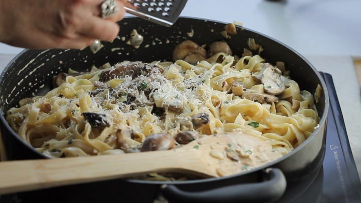 Tagliatelle in a pan covered in a creamy mushroom sauce with grated cheese and fresh cut parsley