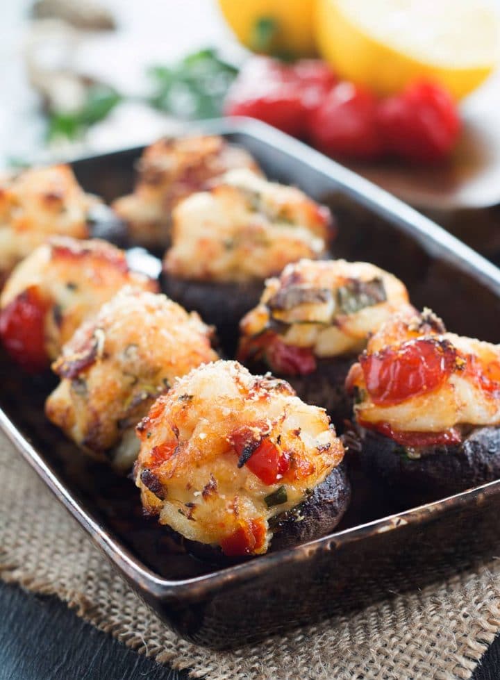 A serving dish filled with easy crab stuffed mushrooms with peppers and lemons in the background