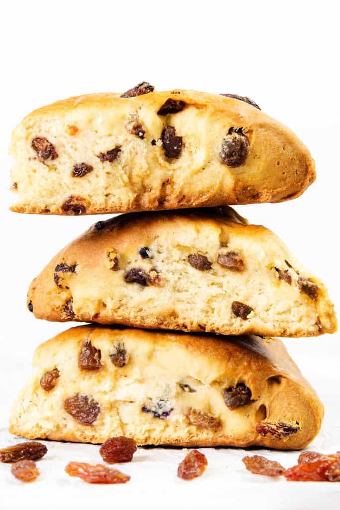 Three thick slices of raisin bread are stacked on top of each other against a white background, with scattered raisins in the foreground—perfect for fans of classic raisin scones.