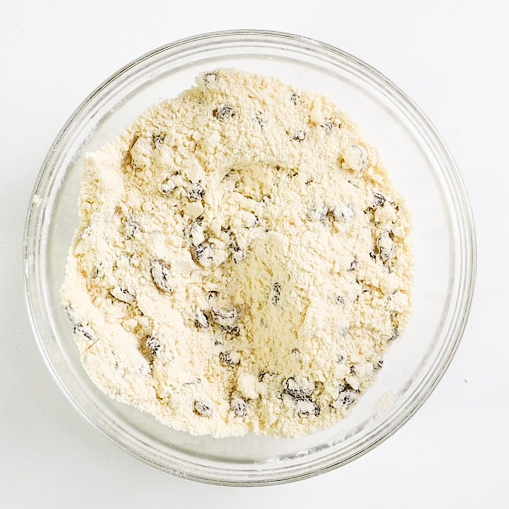 A glass bowl filled with flour and chocolate chips, perfect for making Raisin Scones, viewed from above on a white background.