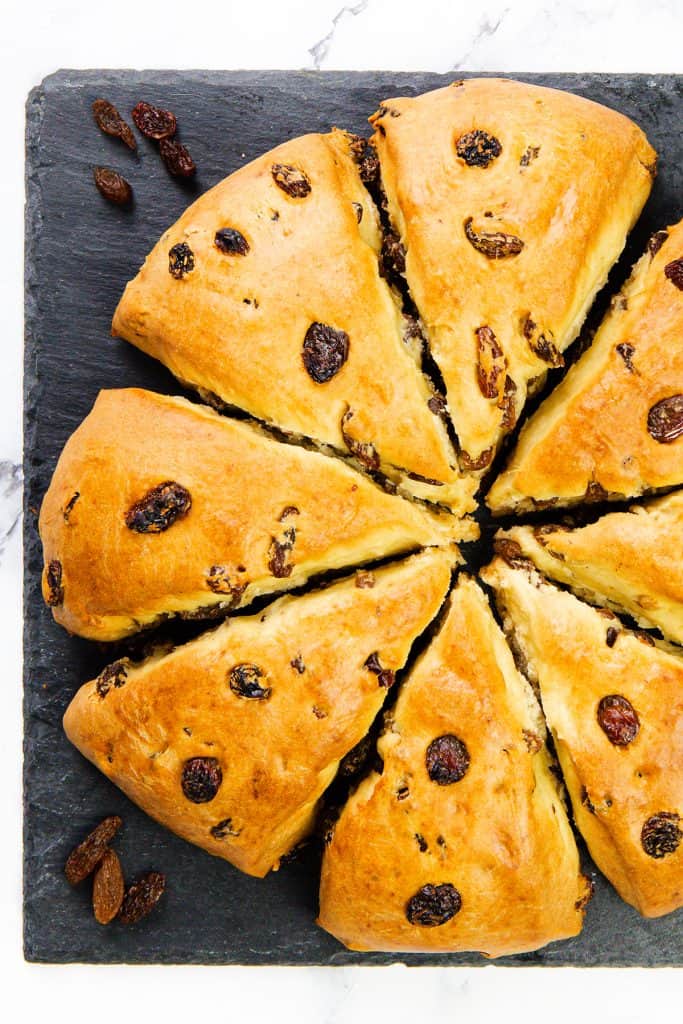 Eight golden-brown Raisin Scones, perfectly triangular, are arranged in a circle on a dark slate surface, with a few loose raisins scattered nearby.
