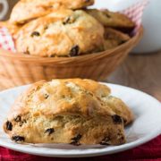 a plate with a raisin scone and a basket of raisin scones in the background