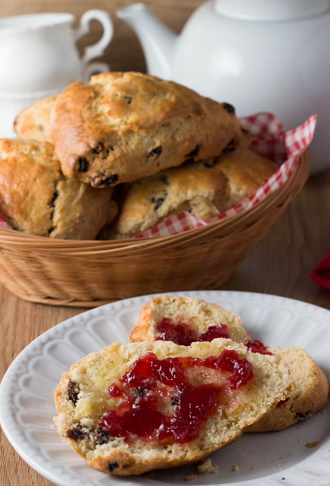 A raisin scone halved with butter and jam, with more raisin scones in the background.