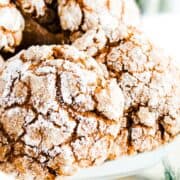 a pile of Ginger Crinkle Cookies on a cake stand with Christmas holly in the background