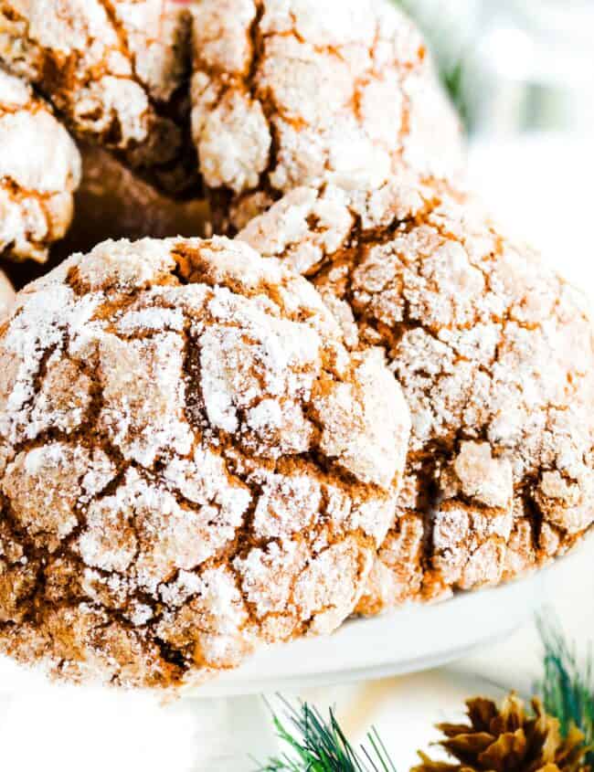 a pile of Ginger Crinkle Cookies on a cake stand with Christmas holly in the background