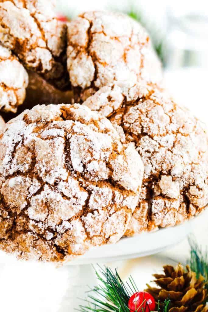 a pile of Ginger Crinkle Cookies on a cake stand with Christmas holly in the background