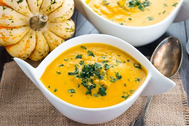 A bowl of Winter Squash Soup topped with fresh parsley with a whole squash and a second bowl in the background 
