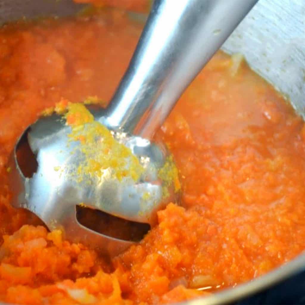 carrot soup being blended with a hand blender