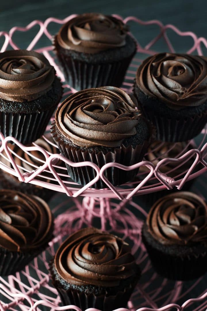 A selection of devils food cupcakes with chocolate icing in a rose swirl on a pink cupcake stand with heart design