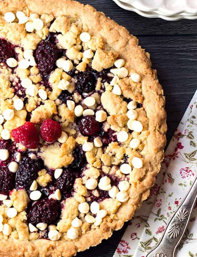 an overhead shot of raspberry and white chocolate shortbread tart with a cake slice on a napkin next to it