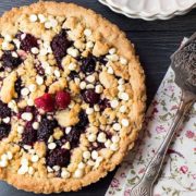 an overhead shot of raspberry and white chocolate shortbread tart with a cake slice on a napkin next to it