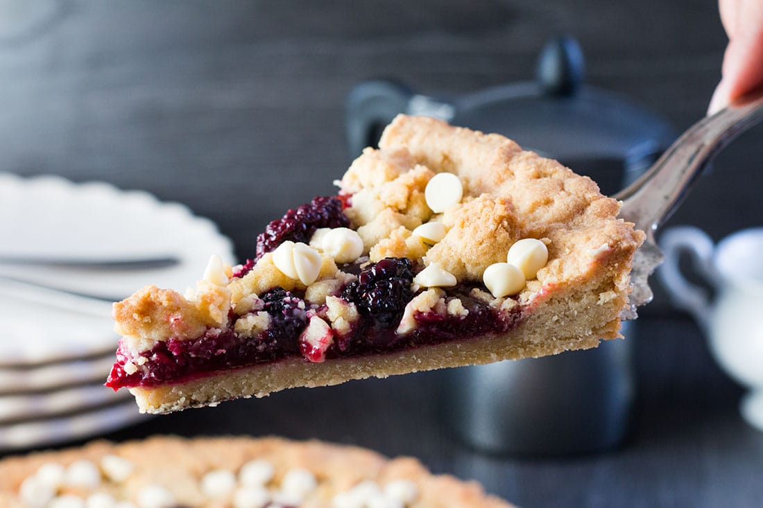 Raspberry and White Chocolate Shortbread Tart slice on cake slice being lifted from the freshly baked pie