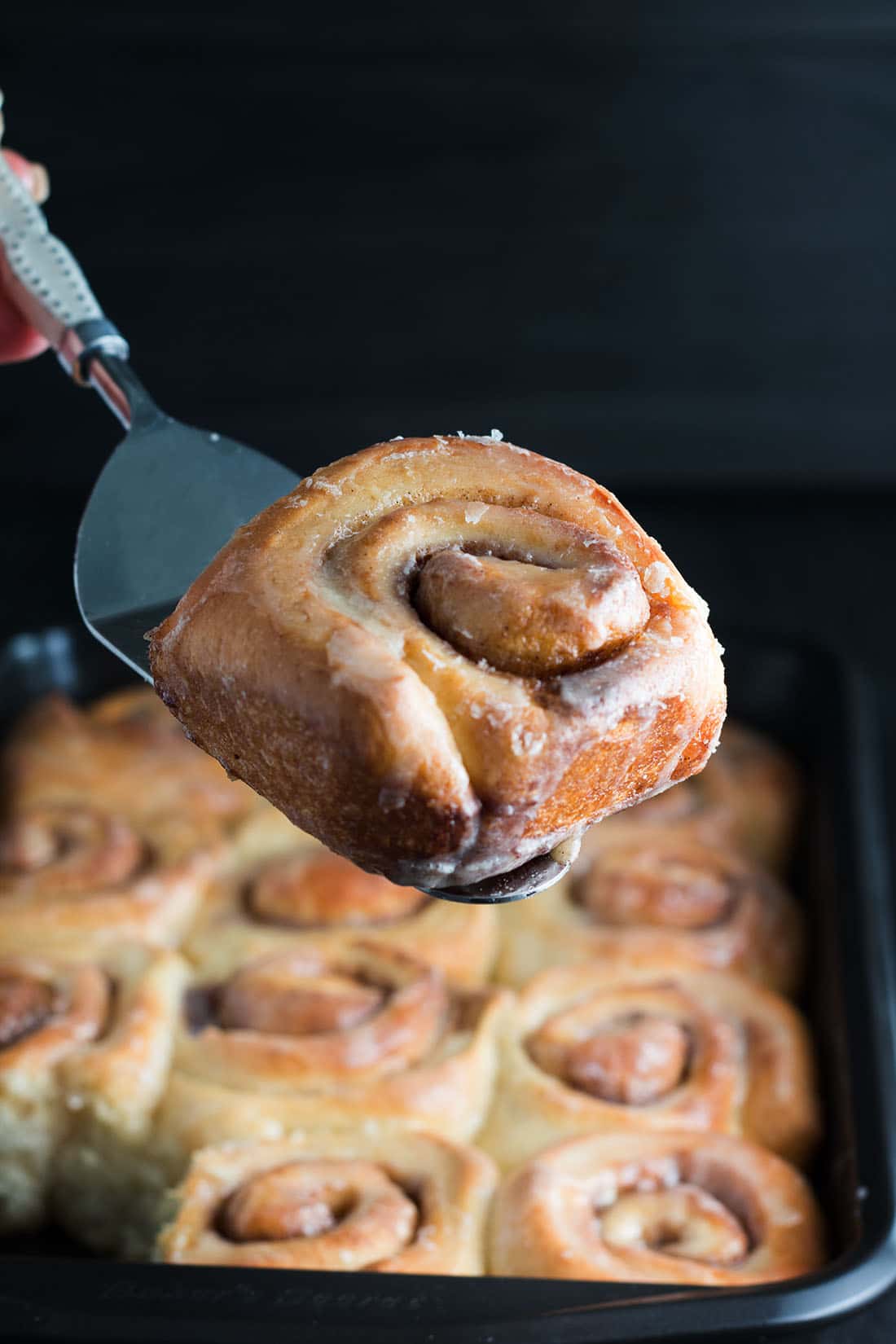 one vanilla bean cinnamon bun being served with the rest of the pan in the background.