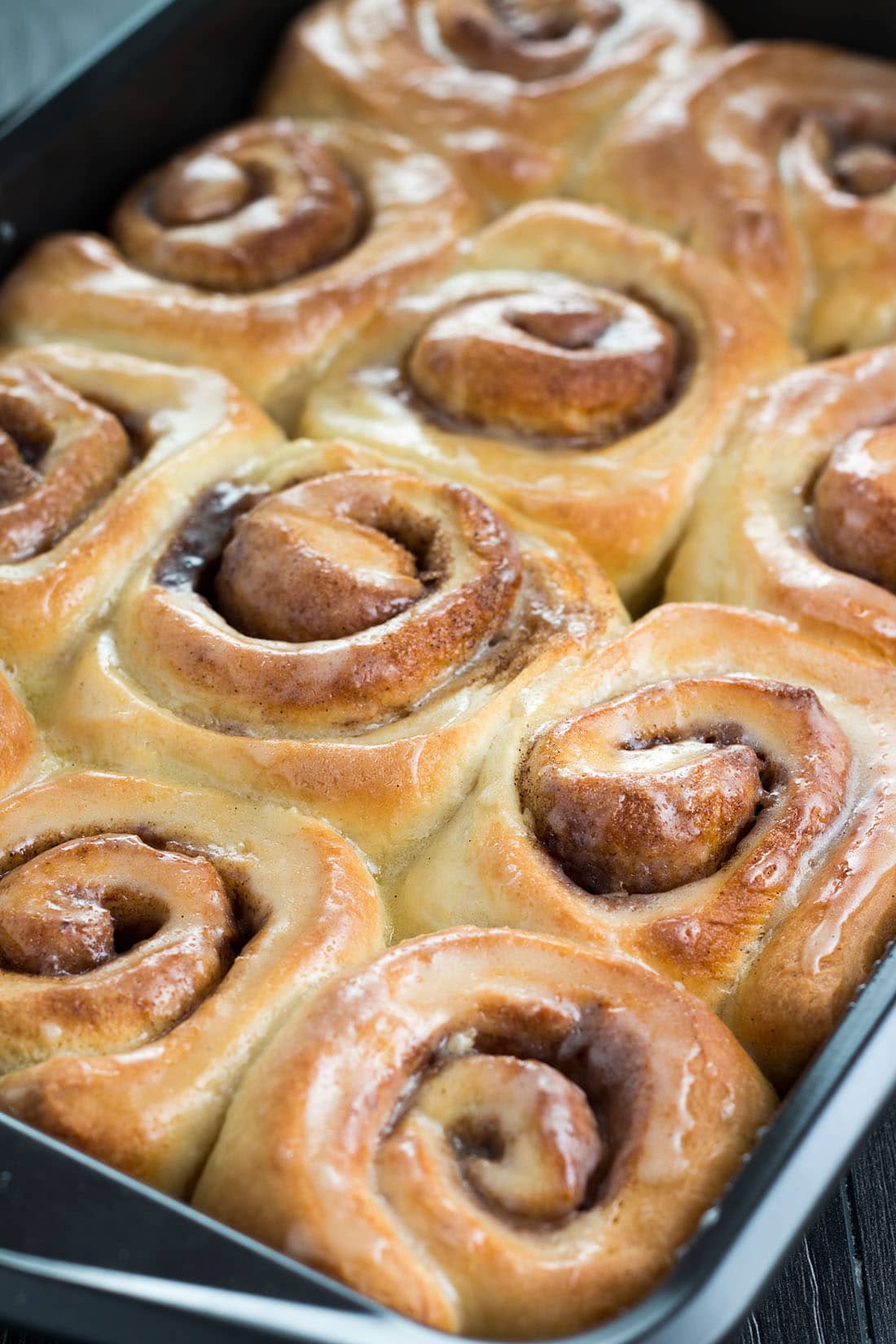 Freshly baked golden brown vanilla bean cinnamon buns in the pan covered with glistening glaze