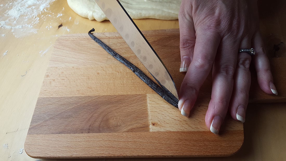 A vanilla pod being sliced down the middle with a knife,