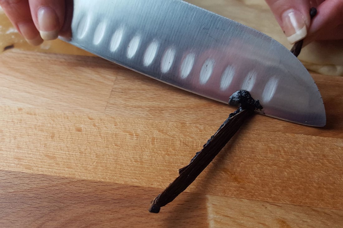 A knife slicing the beans from a vanilla pod 