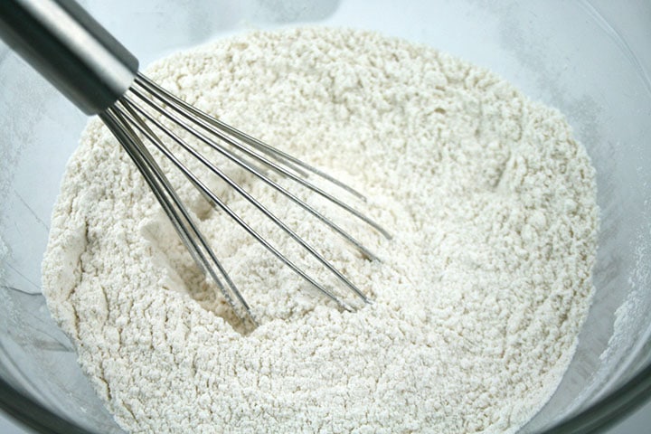 Flour in a mixing bowl with baking powder, and baking soda being mixed in