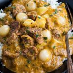 an overhead shot of Beef Massaman curry on a bed of rice in a dish with a fork