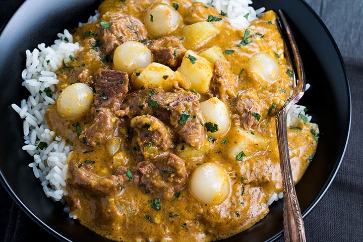 an overhead shot of Beef Massaman curry on a bed of rice in a dish with a fork
