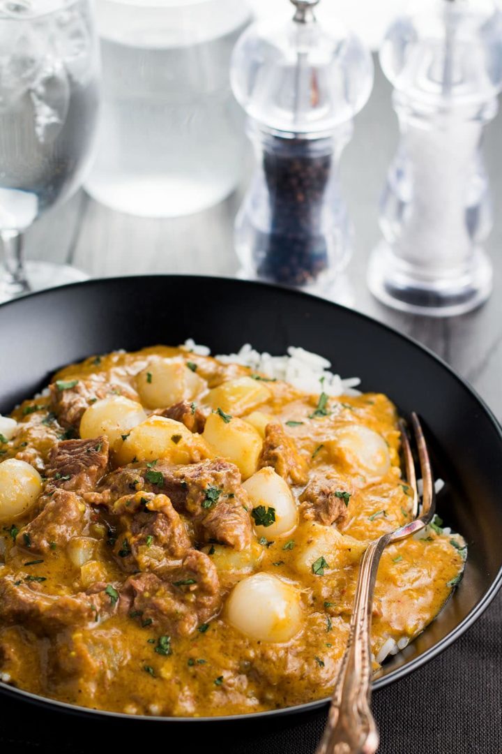 Beef Massaman Thai Curry in a black bowl with a fork and glass or water, salt and pepper mills in the background